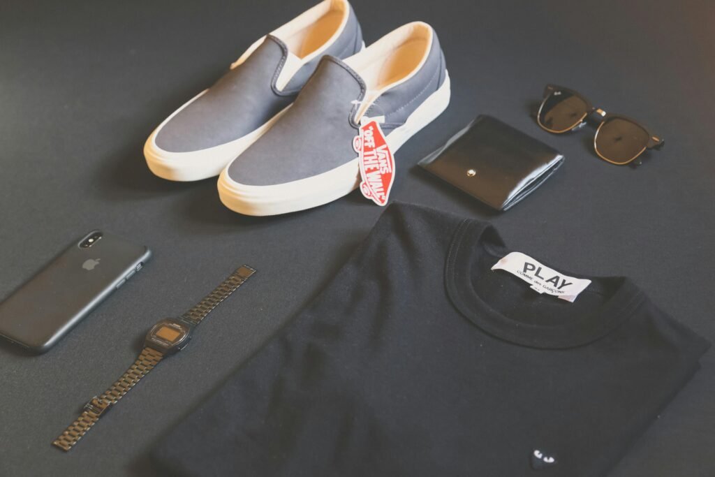 Stylish flat lay of affordable luxury fashion essentials, including sneakers, a designer t-shirt, sunglasses, a wallet, and accessories.