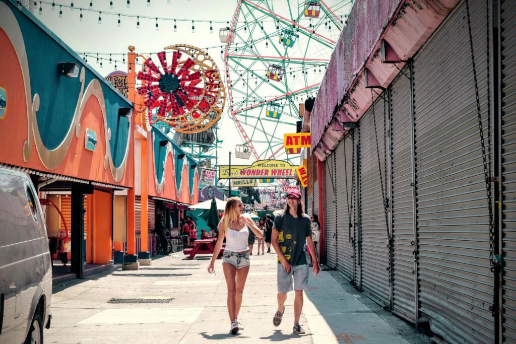 Couple walking through a colorful amusement park with a Ferris wheel in the background.