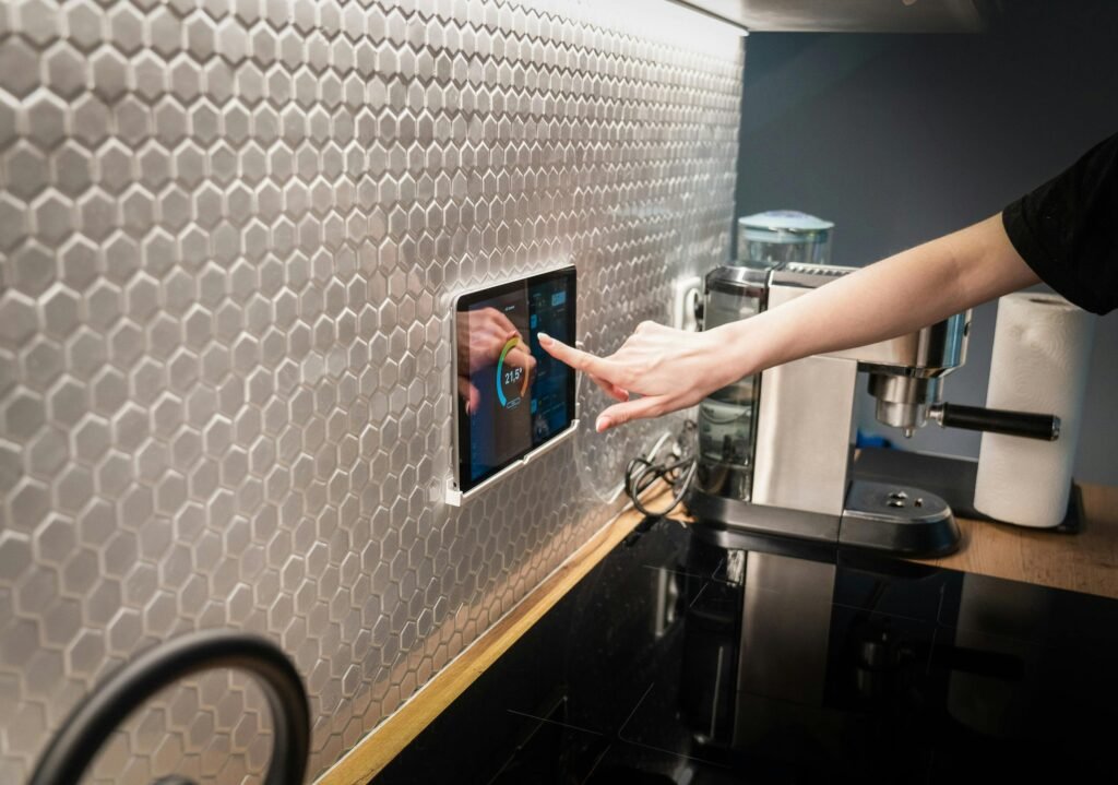 A person using a smart home control panel in a modern kitchen, adjusting temperature settings on a touchscreen device displaying futuristic smart gadgets
